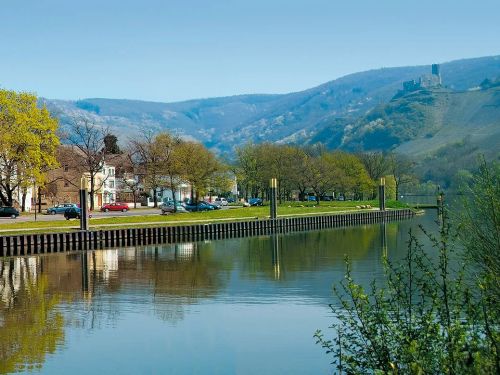 Flussufer mit Häusern Bäumen und Bergen im Hintergrund bei klarem Wetter