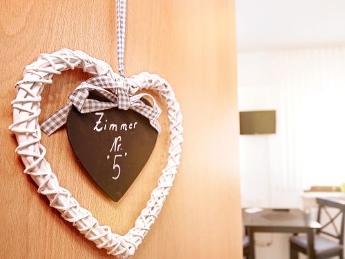 Herzförmiges Schild mit Zimmer Nummer 5 hängt an einer Holztür zum hellen Zimmer