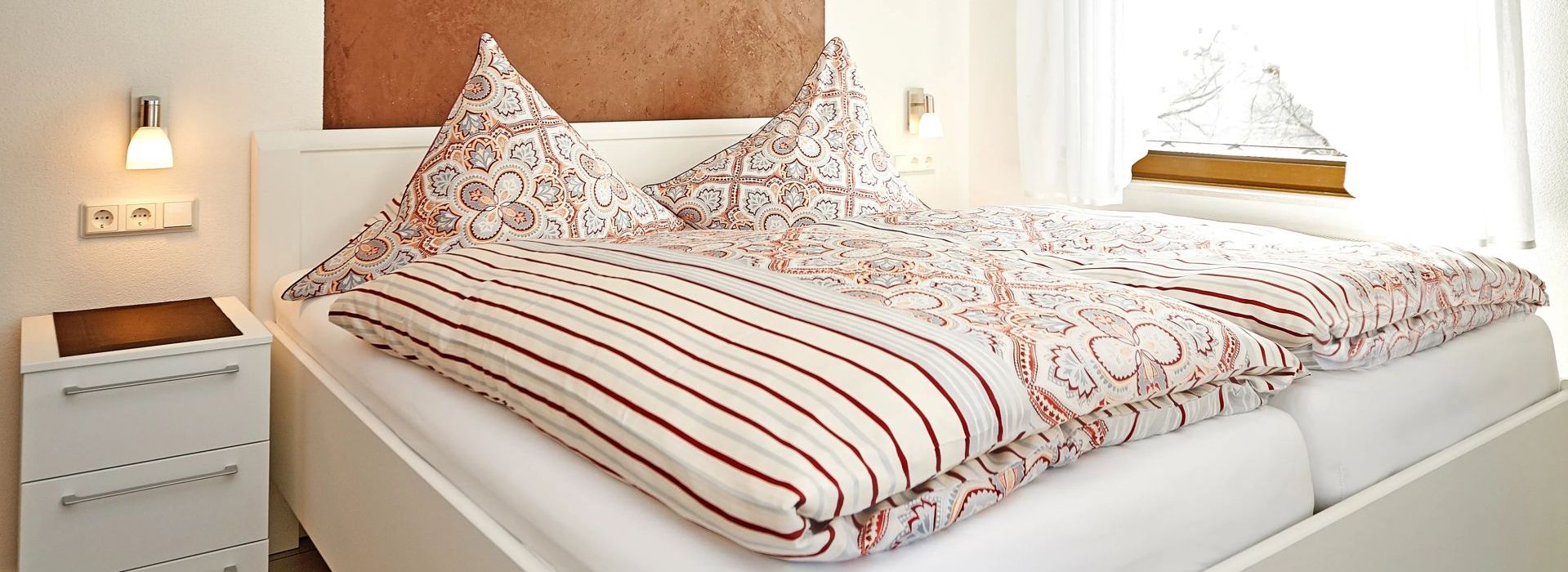 Gemachtes Bett mit gemusterten Kissen und Decken neben einem Nachttisch mit Lampe