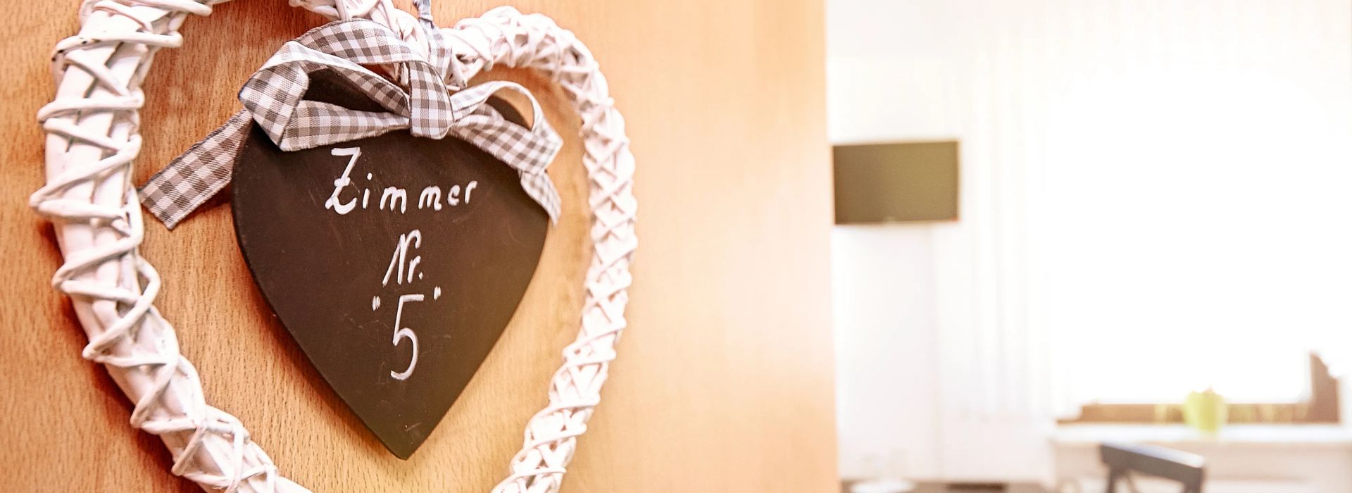 Herz aus weissem geflochtenem Material mit Schild zimmer nummer fünf an Holztuer